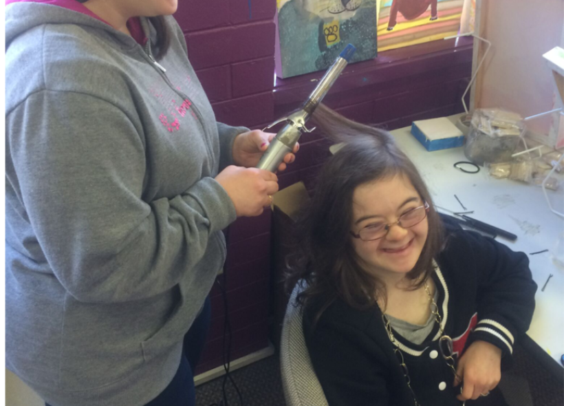 A young woman using curling tongs on another young woman'shair
