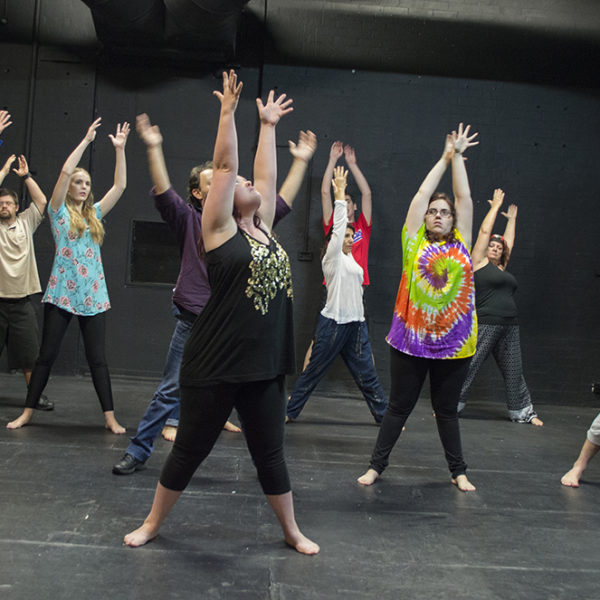 Participants at an Access Arts Theatre & Dance Ensemble workshop dancing and raising their hands up in a rehearsal space.