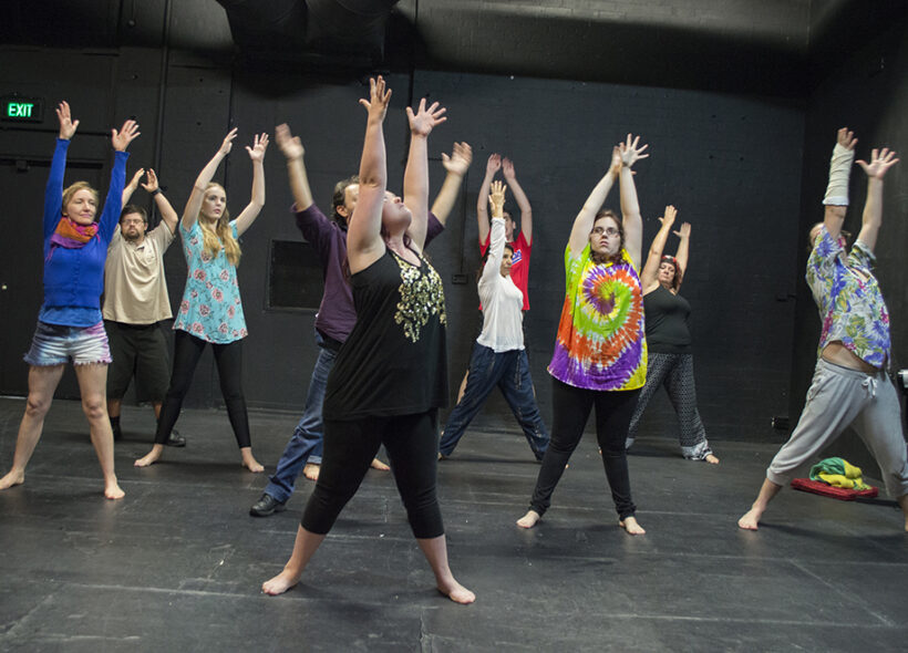 Participants at an Access Arts Theatre & Dance Ensemble workshop dancing and raising their hands up in a rehearsal space.
