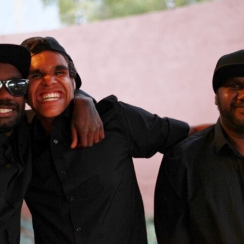3 young smiling aboriginal men standing front of a curved pink wall