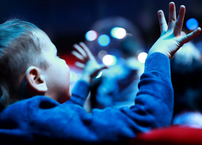 Young boy in cinema. Hands in the air.