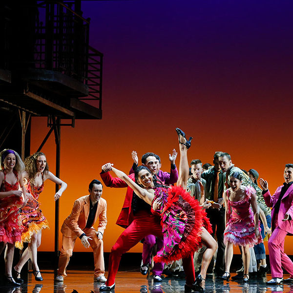 A group of people dance wearing colourful dresses and suits.