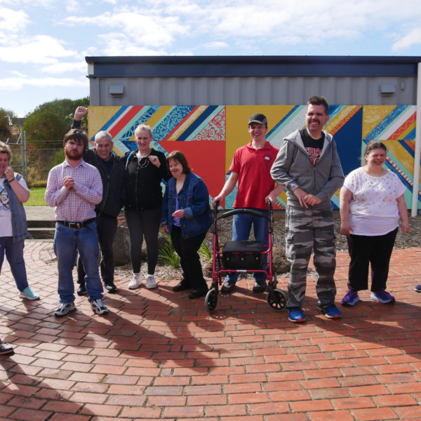 A group shot of the Art About artists infront of a brightly coloured mural. 