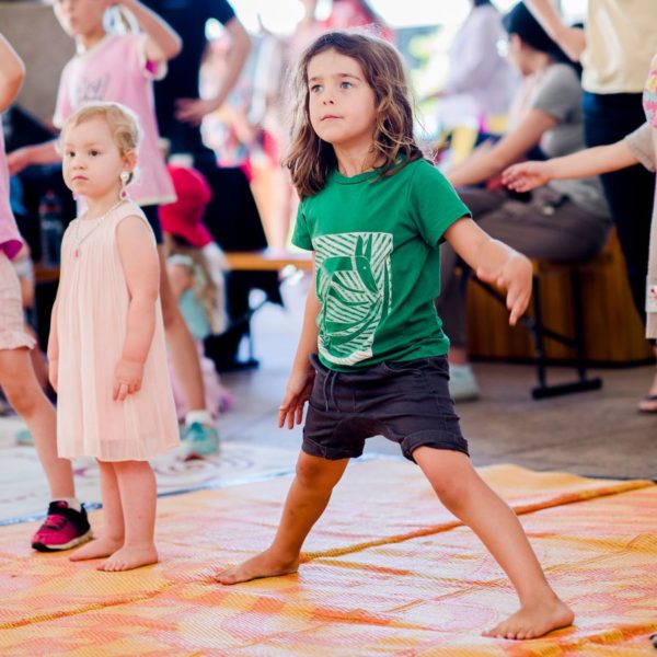 Three young children in brightly dressed summer clothing, standing in different poses looking ahead for movement instructions