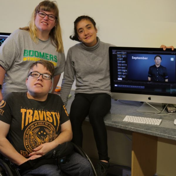Three people sitting near computers.