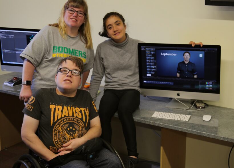Three people sitting near computers.
