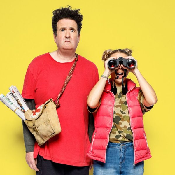 Actor Alan Brough holding bag of rolled up newspapers and female actress with binoculars over her face 