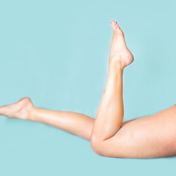 A pair of legs with a vivid blue background. A pair of purple velvet underwear can be seen.