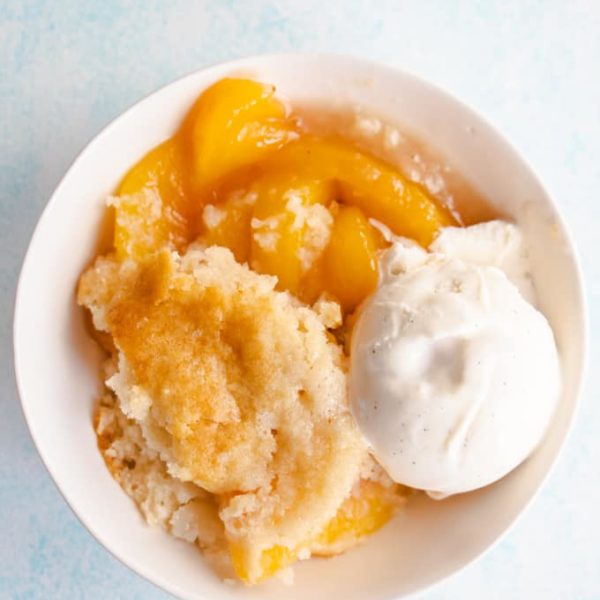 A bowl of ice cream and peach cobbler on a plain white background