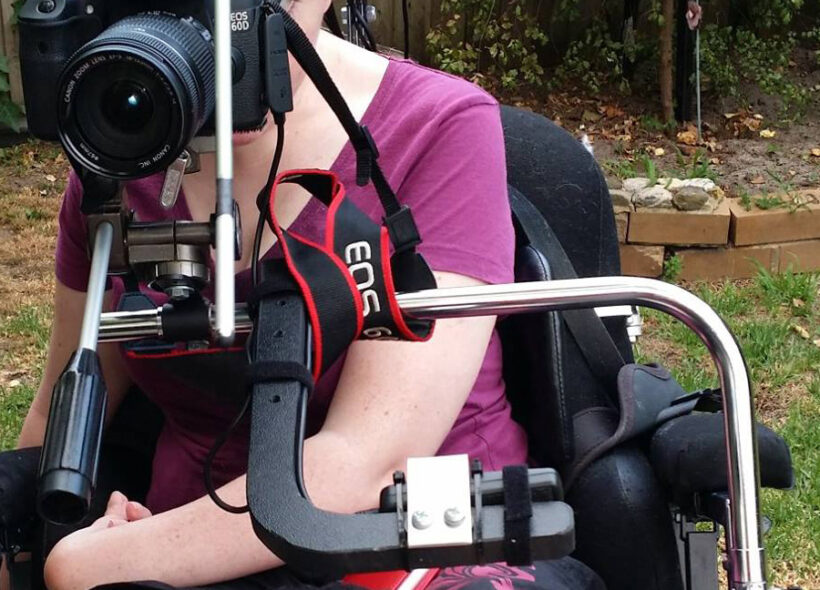 Woman in wheelchair in pink shirt looking through a camera lens