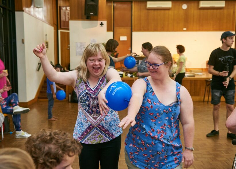Two people laughing and holding a balloon between their arms. 