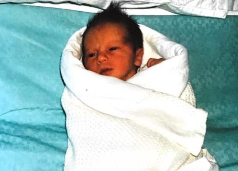 A newborn baby wrapped in a white cloth, lying on a blue blanket.