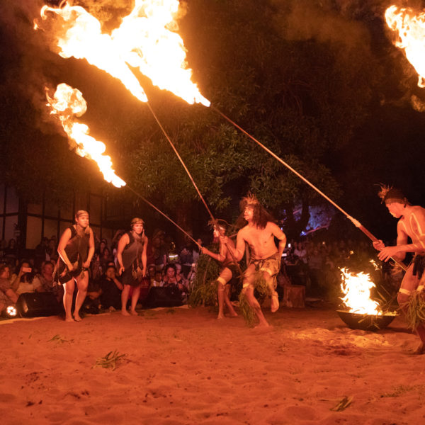 Red ochre sand. Indigenous men holding long fire sticks.