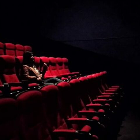 A person is sitting in a darkly lit theatre.