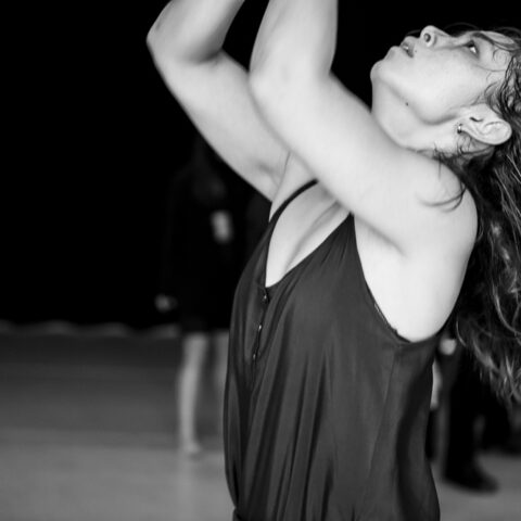 A close up of a dancer looking up with arms raised in black and white