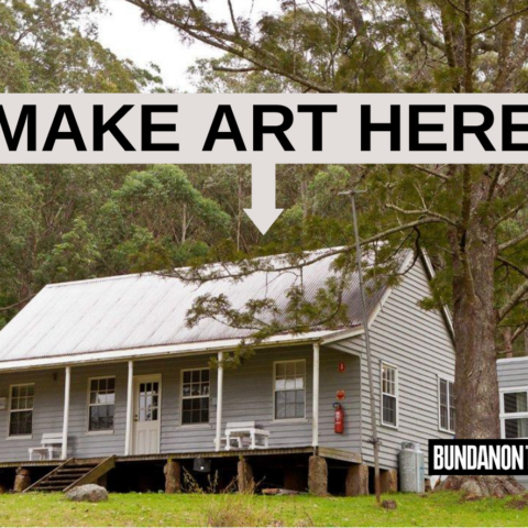 A promotional image of the Bundanon Trust estate. The image contains a single white/grey house in the middle of the bush during day time. There is grass and big trees surrounding the house and there’s a copied and pasted sign just on top of the roof of the house that reads – MAKE ART HERE with an arrow pointing down at the house in big bold black font. In the bottom right corner there is the Bundanon Trust logo in big bold white font with a black background and the Accessible Arts logo in small white font and a bright pink background.