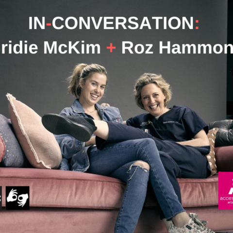 Two women are sitting on a pink velvet couch. The woman on the left has long light brown hair pulled back in a ponytail and is wearing denim jeans and jacket. The woman on the right has mid length light brown hair and is wearing a navy blue top and pants.