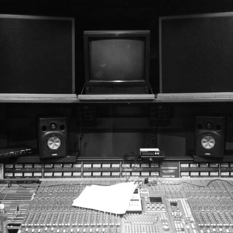 A black and white group image of a large audio mixing desk with speakers and screens.