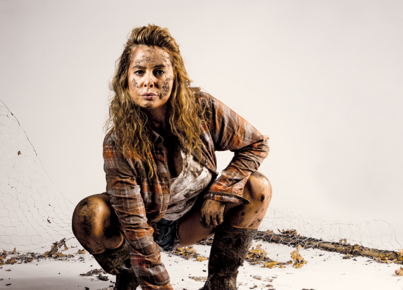 A woman, covered in dirt is bending down as if ready to pounce