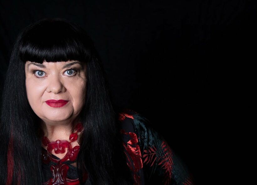 Portrait photo of Lynette Wallworth against a black background. She has black hair with a fringe and is wearing red lipstick and a red necklace.