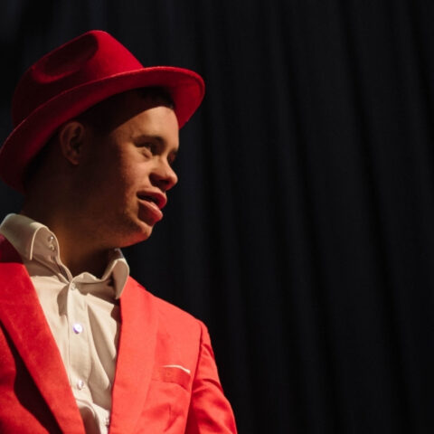 Strangeways Ensemble member Ethan Green in a red suit with a matching red fedora.