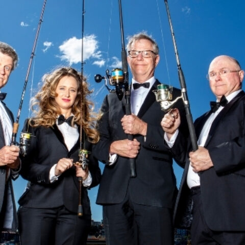 The cast of the Wharf Revue (L-R: Drew Forsythe, Mandy Bishop, Jonathan Biggins and Phil Scott) wear black tuxedo jackets and stand against a blue sky holding fishing rods.