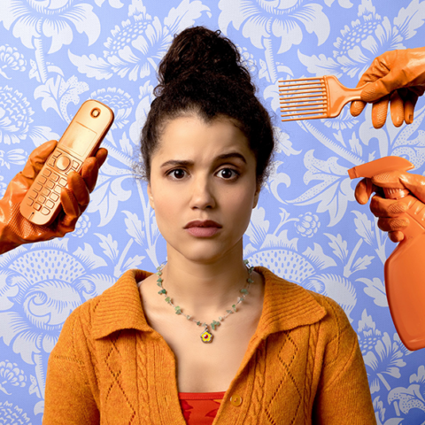 woman in a high bun and orange cardigan, looks concerned as there are orange gloved arms around her head