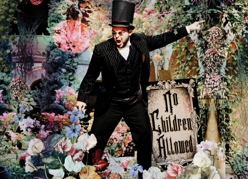The Selfish Giant man in a black suit and top hat, standing amongst a field of flowers in his garden, angrily pointing beside a sign that reads 'no children allowed'.