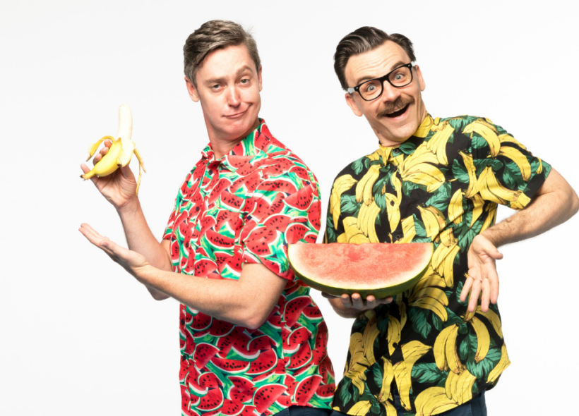 Two performers stand in bright coloured shirts holding a banana and a watermelon