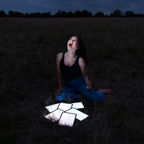 A woman in a dark field with lit up tables devices in front of her