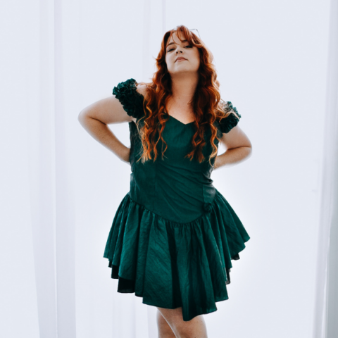 Young woman with red hair in a green dress with her hands on her hips