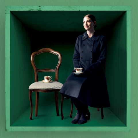 Woman sitting on a brown chair in a green box enjoying a cup of tea.