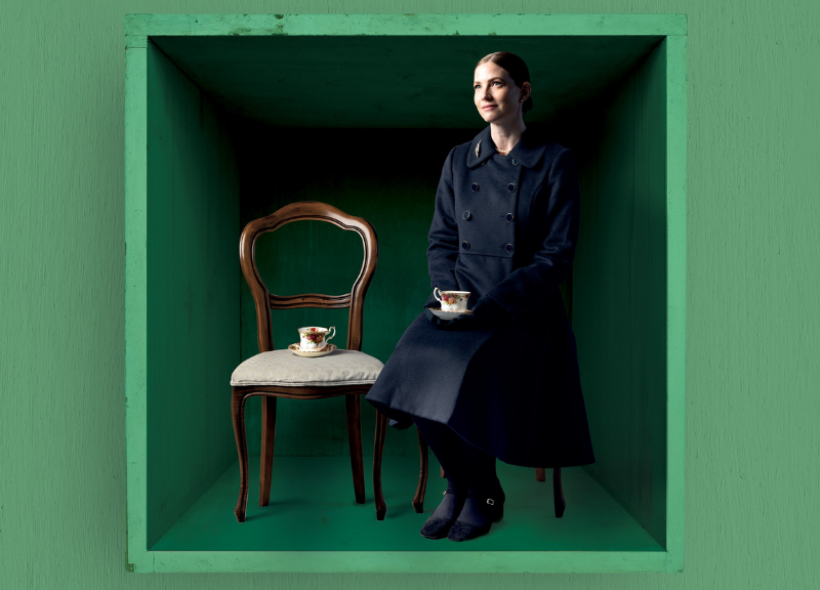 Woman sitting on a brown chair in a green box enjoying a cup of tea.
