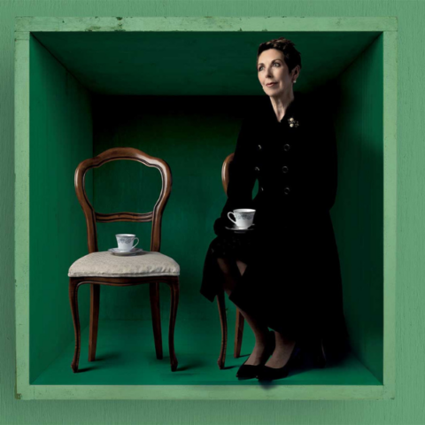 Woman sitting on a brown chair in a green box enjoying a cup of tea.