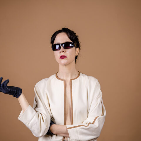 A woman poses nonchalantly while wearing sunglasses and a pair of black gloves  