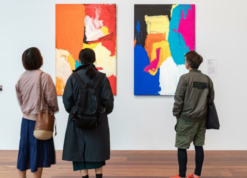Three people looking at two pieces of colourful abstract art.