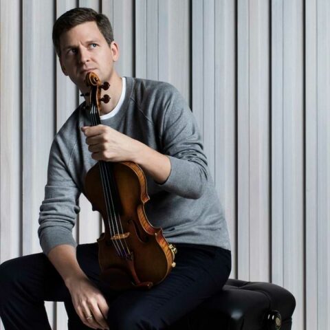 James Ehnes sits on stool and holds violin 