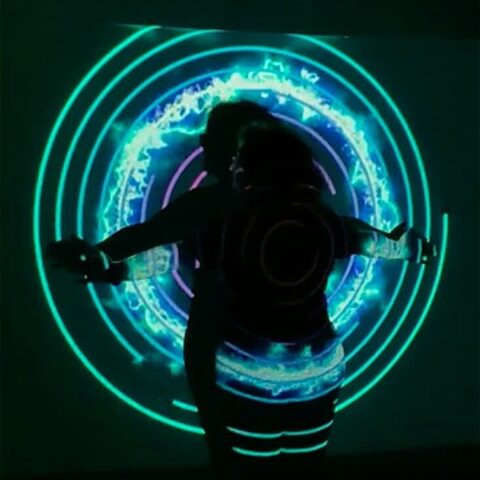Performer standing in front of white screen being lit by projections of circles and light
