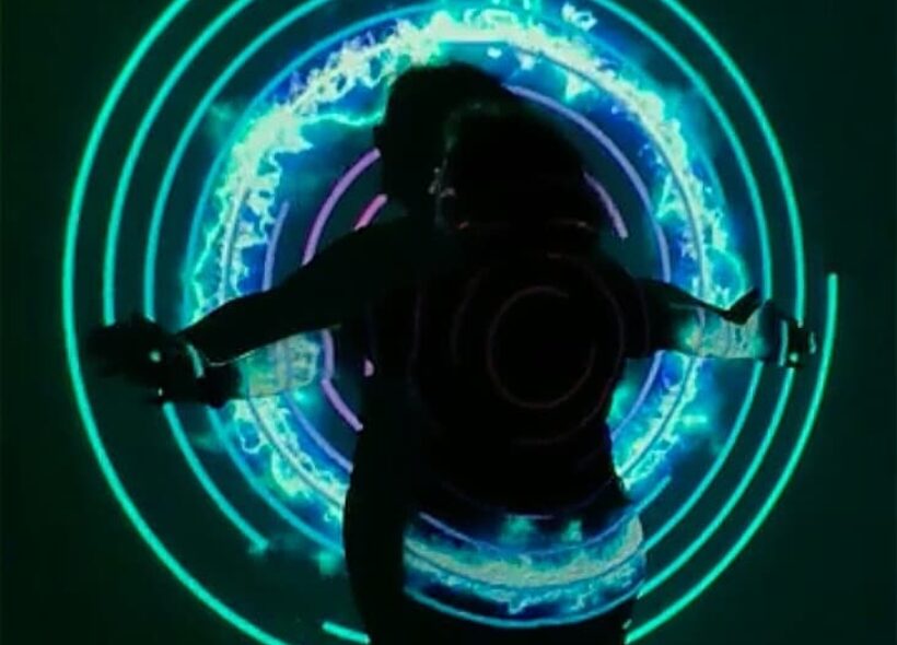 Performer standing in front of white screen being lit by projections of circles and light