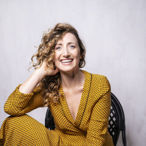 Woman with curly blonde hair in a yellow dress sitting on a chair