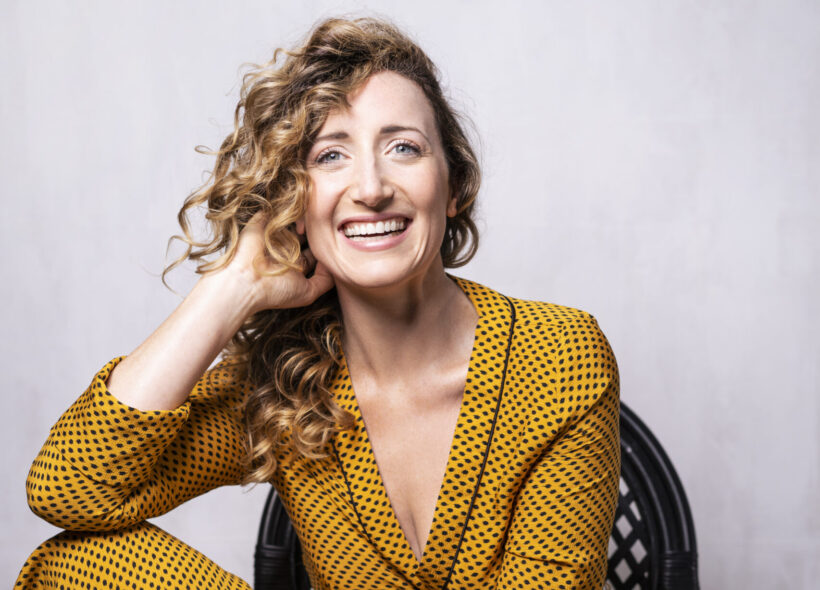 Woman with curly blonde hair in a yellow dress sitting on a chair