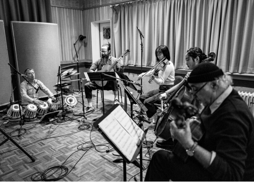Black and white image of musicians in a recording studio with guitars, violin, cello and tablas