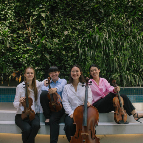 Four women in black pants and shirts sitting in front of a pool with string instruments