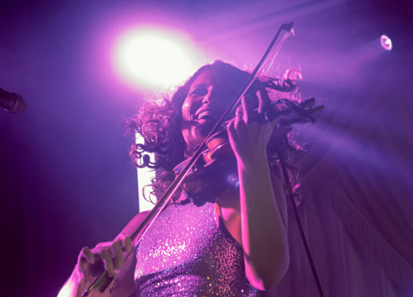 women playing violin on stage with bright purple lights