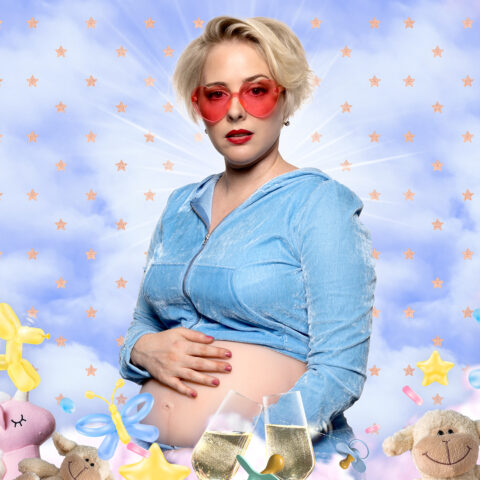 A blonde pregnant woman wearing a blue tracksuit holds her belly and stares to camera. She is surrounded by Baby Borns and other baby toys and is photoshopped onto a cloudy blue sky backdrop.