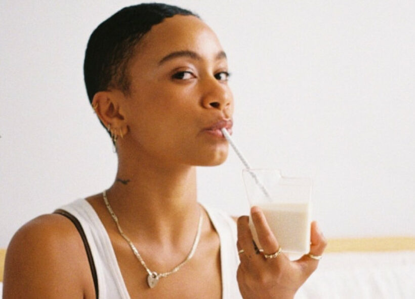 Aurelia St Clair in a white top in front of a white background sipping a glass of milk or non-dairy beverage with a straw.