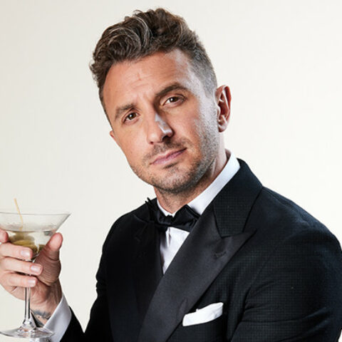 Tommy Little in a suit and bowtie holding a martini with olives in it.