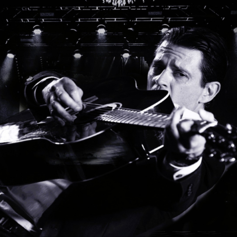 Black and white image of a man playing a black acoustic guitar