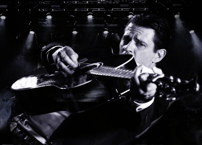 Black and white image of a man playing a black acoustic guitar