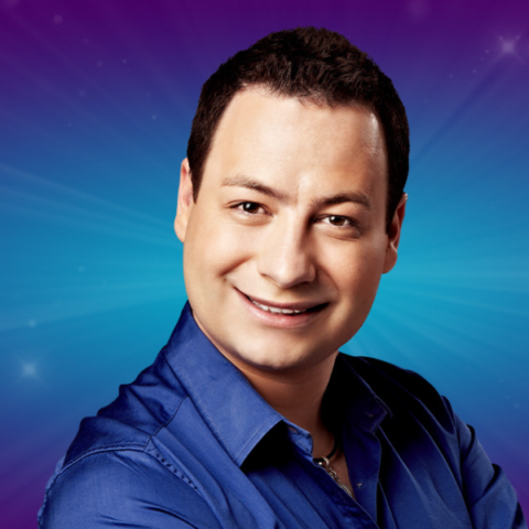 Man in blue shirt smiling in front of a blue sparkled backdrop.